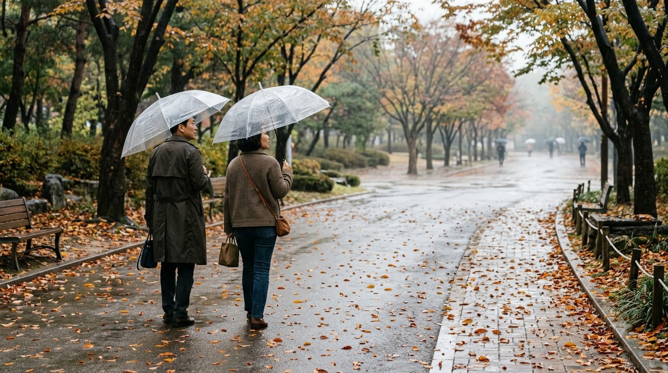 투명 우산을 쓰고 젖은 가을 공원길을 걷는 두 사람